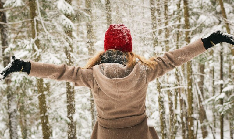 Girl standing backwards with hands in air facing a snow covered forest