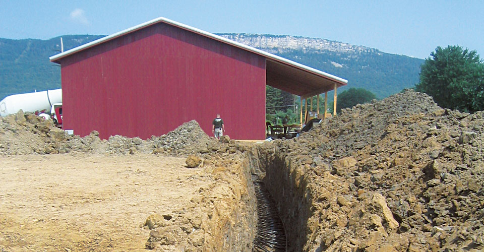 Photo of red building and trench-in-progress, at Whitecliff Vineyard, with Shawangunk mountains in the background.