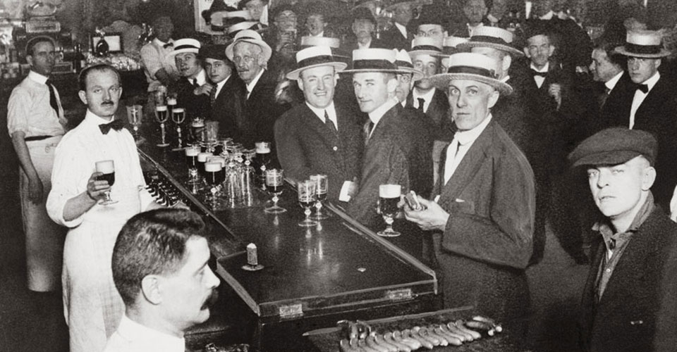 Vintage black & white photo of the interior of a crowded bar moments before midnight, June 30, 1919, when wartime prohibition went into effect, in New York City.