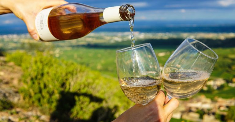 Photo of white wine being poured into two glasses, held by one hand.
