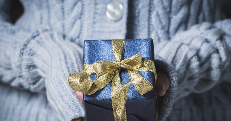 girl in blue sweater holding blue gift wrapped package with gold ribbon