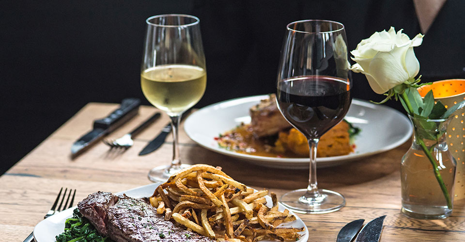 closeup of plated food set up with two wine glasses on wooden table