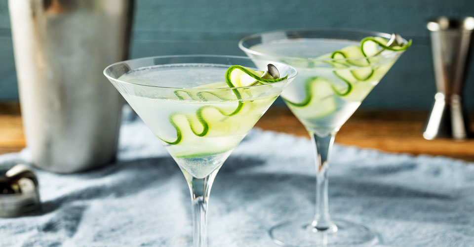 two sake martini glasses with cucumber ribbon garnish on a blue napkin