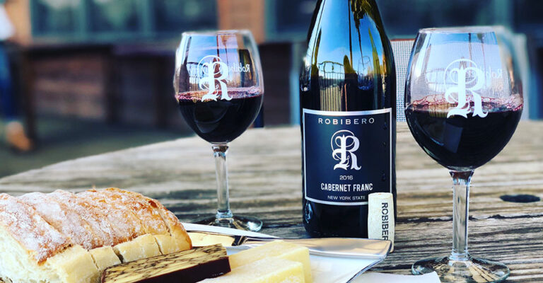 bottle of wine and two glasses with plate of cheese on wooden table