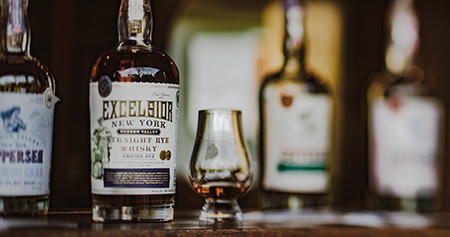four bottles of whiskey and a small glass on a dark wood bar