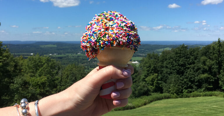 close-up of ice cream cone with multi-colored sprinkles against blue sky